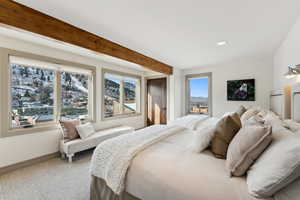 Carpeted bedroom featuring beam ceiling and multiple windows