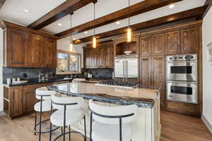 Kitchen featuring light hardwood / wood-style flooring, dark stone countertops, beam ceiling, appliances with stainless steel finishes, and a kitchen island