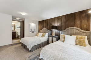 Carpeted bedroom featuring connected bathroom and wooden walls