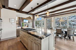 Kitchen featuring stainless steel gas cooktop, beam ceiling, a center island, a stone fireplace, and hanging light fixtures