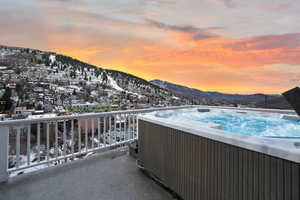 Snow covered back of property with a mountain view and a hot tub