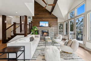 Living room with wood walls, high vaulted ceiling, hardwood / wood-style flooring, ceiling fan, and a fireplace