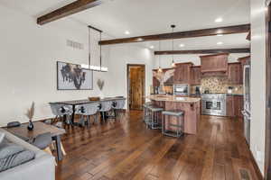 Kitchen with light stone counters, dark wood-type flooring, stainless steel appliances, and decorative light fixtures