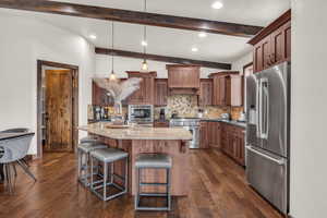 Kitchen with light stone counters, stainless steel appliances, dark hardwood / wood-style floors, hanging light fixtures, and an island with sink