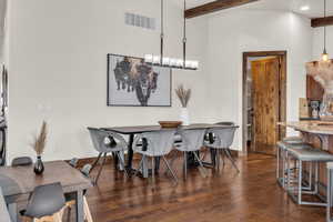 Dining space featuring dark hardwood / wood-style floors, beam ceiling, a towering ceiling, and a chandelier