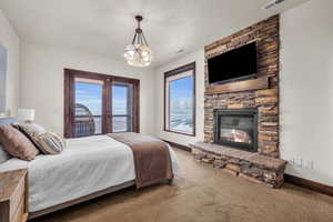 Carpeted bedroom with a stone fireplace and access to exterior