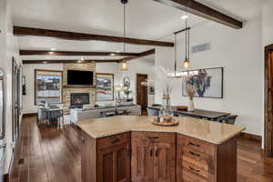 Kitchen with dark wood-type flooring, beam ceiling, a fireplace, a kitchen island, and hanging light fixtures