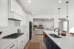 Kitchen with white cabinetry, sink, stainless steel gas cooktop, decorative light fixtures, and light wood-type flooring