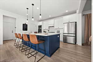 Kitchen featuring white cabinetry, light wood-type flooring, an island with sink, and appliances with stainless steel finishes