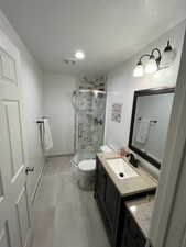 Bathroom featuring vanity, a shower with shower door, a textured ceiling, and toilet