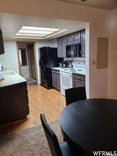 Kitchen with gray cabinetry, sink, light hardwood / wood-style flooring, electric panel, and black appliances