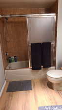 Bathroom with shower / bath combination with glass door, hardwood / wood-style floors, and toilet