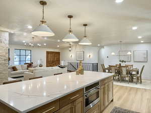 Kitchen featuring light stone countertops, a center island, light hardwood / wood-style flooring, and hanging light fixtures