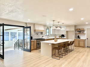 Kitchen with a kitchen island, light wood-type flooring, high end stove, and custom range hood