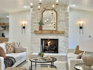 Living room featuring hardwood / wood-style floors, a textured ceiling, a stone fireplace, and a notable chandelier