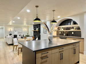 Kitchen featuring a center island, hanging light fixtures, a textured ceiling, a fireplace, and light hardwood / wood-style floors