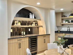 Bar with decorative backsplash, light brown cabinetry, sink, light hardwood / wood-style flooring, and wine cooler