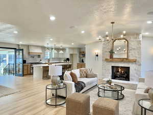 Living room featuring a textured ceiling, light wood-type flooring, an inviting chandelier, and a stone fireplace