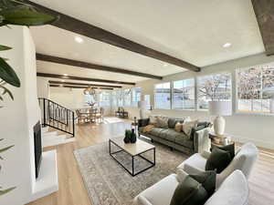 Living room featuring beam ceiling, light wood-type flooring, a textured ceiling, and a wealth of natural light