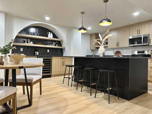 Bar with light brown cabinetry, backsplash, wine cooler, and hanging light fixtures