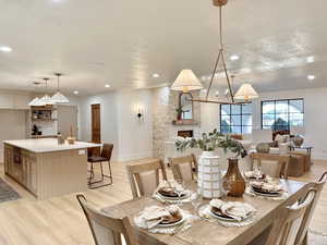 Dining room with a stone fireplace, light wood-type flooring, and a textured ceiling