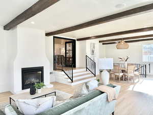 Living room with a large fireplace, beamed ceiling, and light wood-type flooring