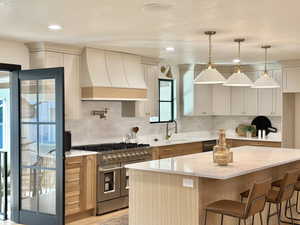 Kitchen with a kitchen island, stainless steel appliances, decorative light fixtures, and custom exhaust hood