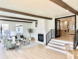 Living room featuring beam ceiling, a fireplace, light hardwood / wood-style floors, and a textured ceiling