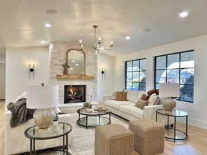 Living room featuring a textured ceiling, light hardwood / wood-style flooring, a stone fireplace, and a notable chandelier