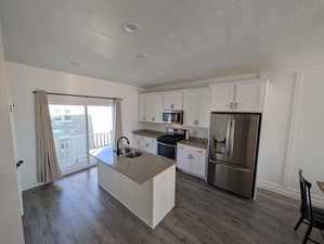 Kitchen with white cabinets, appliances with stainless steel finishes, a kitchen island with sink, and sink