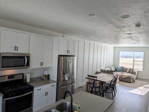 Kitchen with white cabinets, sink, light wood-type flooring, a textured ceiling, and appliances with stainless steel finishes