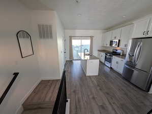 Kitchen featuring appliances with stainless steel finishes, dark wood-type flooring, sink, white cabinetry, and an island with sink