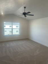 Carpeted empty room featuring ceiling fan, a textured ceiling, and vaulted ceiling