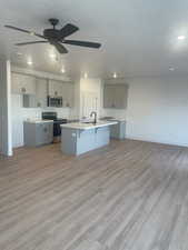 Kitchen with appliances with stainless steel finishes, a center island with sink, gray cabinetry, and light hardwood / wood-style floors