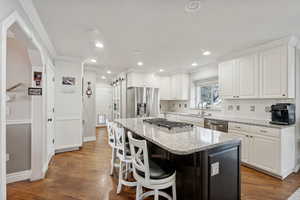 Kitchen with light stone countertops, appliances with stainless steel finishes, dark wood-type flooring, white cabinets, and a kitchen island