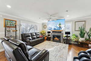 Living room with a fireplace, crown molding, hardwood / wood-style floors, and ceiling fan