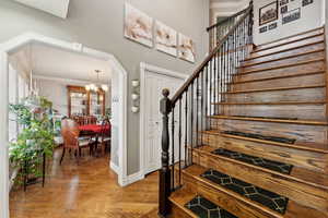 Staircase with hardwood / wood-style floors, ornamental molding, and a notable chandelier