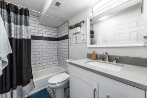 Full bathroom with shower / bath combination with curtain, vanity, a textured ceiling, and toilet