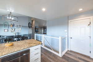 Kitchen featuring white cabinets, light stone counters, hanging light fixtures, and dark wood-type flooring