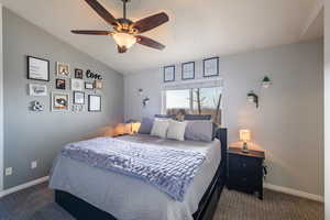 Bedroom featuring ceiling fan, lofted ceiling, and dark colored carpet