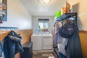 Laundry area featuring a textured ceiling, dark wood-type flooring, wooden walls, and washing machine and clothes dryer