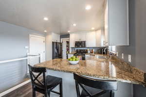 Kitchen featuring kitchen peninsula, sink, appliances with stainless steel finishes, dark hardwood / wood-style flooring, and white cabinetry