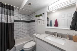 Full bathroom featuring vanity, toilet, shower / bath combo with shower curtain, and a textured ceiling