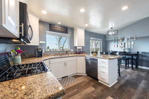 Kitchen featuring range, kitchen peninsula, dark hardwood / wood-style floors, black dishwasher, and white cabinetry