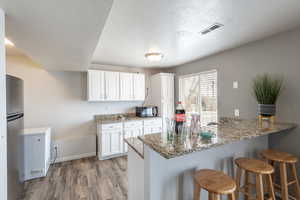 Kitchen with kitchen peninsula, hardwood / wood-style floors, white cabinetry, and stainless steel refrigerator