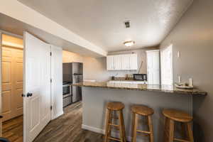 Kitchen with dark stone counters, kitchen peninsula, appliances with stainless steel finishes, dark hardwood / wood-style flooring, and white cabinetry