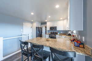 Kitchen featuring kitchen peninsula, appliances with stainless steel finishes, white cabinets, dark hardwood / wood-style floors, and a breakfast bar area