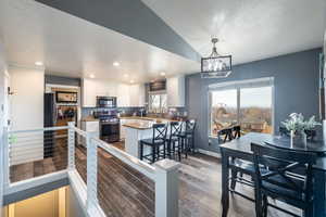 Kitchen with a kitchen bar, stainless steel appliances, wood-type flooring, pendant lighting, and white cabinets