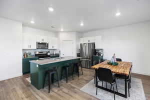 Kitchen featuring a breakfast bar, a center island with sink, light wood-type flooring, white cabinetry, and stainless steel appliances