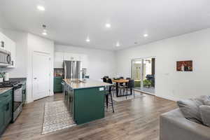 Kitchen featuring white cabinets, a kitchen breakfast bar, a kitchen island with sink, and appliances with stainless steel finishes